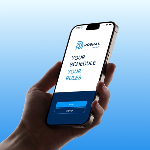 A hand holding a smartphone with the screen displaying a login page for Roshal Health